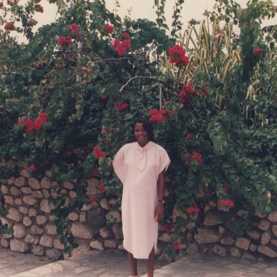 Photo of a beautiful woman in a pink dress standing beside pink flowers in Haiti
